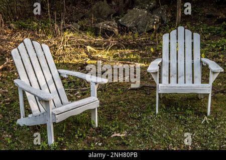 Two white Adirondack chairs with light streaming behind and rocks in the background on a spring day in Taylors Falls, Minnesota USA. Stock Photo