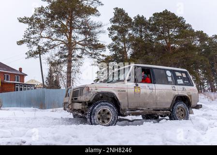 Offroad SUV 'Mitsubishi Pajero' 4x4 rides on a snowy road in the forest among pines in winter. Stock Photo