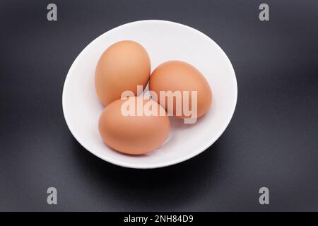 Three chicken eggs in a white bowl against a black background Stock Photo