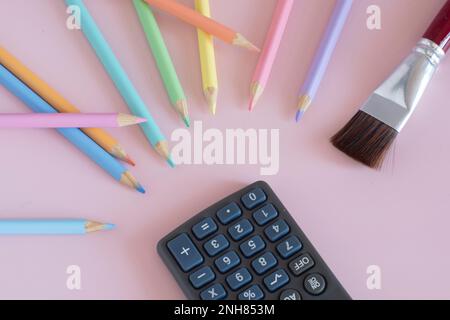 Pastel colored pencils with a brush and a calculator, top view on pink background, back to school concept Stock Photo