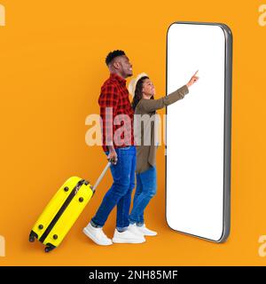 Cheery millennial black couple with suitcase, using big smartphone, mockup Stock Photo
