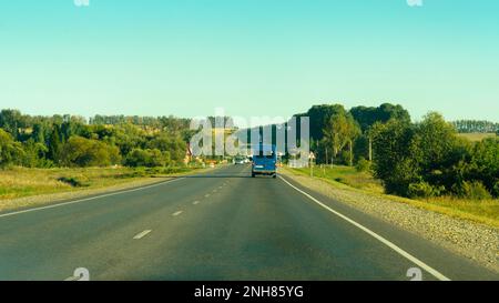 look through the car window. Unknown vechicles driving on the road among fields and woods in summer in Stock Photo