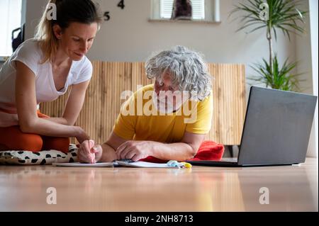 Young woman teaching a senior man how to use laptop computer in a conceptual image of one generation helping the other to develop and modernize. Stock Photo