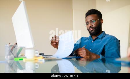 Focused young black businessman using computer and analyzing marketing report, sitting at workplace in office, panorama Stock Photo