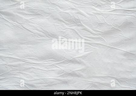 Blank white crumpled and creased paper. White sheet of crumpled paper glued to the wall. Beautiful abstract artistic white empty street poster paper t Stock Photo