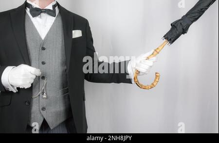 Portrait of Butler or Concierge in Dark Suit and White Gloves Holding Umbrella. Service Industry and Professional Hospitality. Stock Photo