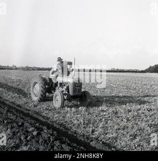 1965, historical, a farmer, in a shirt & tie, jacket and hat standing on a tractor, beside a lady driver, Barton, England, UK. The woman is having a lesson on how to plough a field. The tractor is a Massey-Ferguson 35X, a classic model of the era. Stock Photo