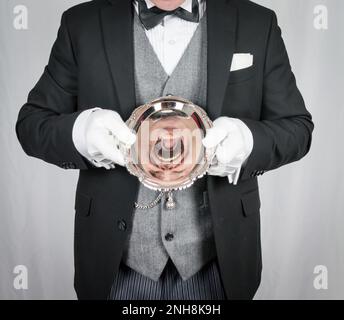 Portrait of Butler or Waiter in Dark Formal Suit Holding Serving Tray and Screaming. Concept of The Butler Did It. Stock Photo