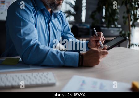 Close up view of the man in shirt touching tablet screen with stylus while sitting at the table Stock Photo