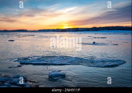 Reflection of the sunset in the icy Lielupe River. Cracked ice on the river. Thaw. Stock Photo