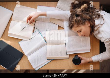 Tired student got asleep on the desk while studying among books Stock Photo