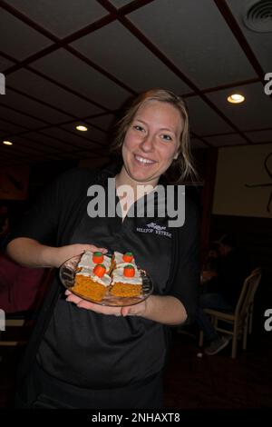 Waitress smiling serving a plate of Halloween cakes decorated with pumpkin candy at the Hilltop Restaurant on Sand Lake. Cumberland Wisconsin WI USA Stock Photo