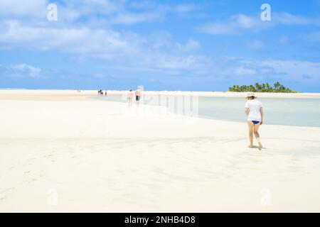 Aitutaki Cook Islands - November 7 2010; Tourists walking in distance on tidal patterned coral sand atoll, under blue sky with puffy white clouds Stock Photo