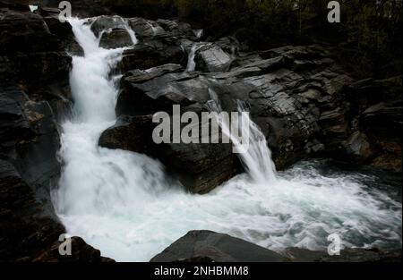 A small, creek, brook, flows over the dark cliff at a slope. Beautiful and dramatic place. Stock Photo