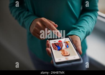 Close-up of person using mobile phone for internet use. Young man holds his finger on the smartphone screen and puts like on photo portrait on social Stock Photo