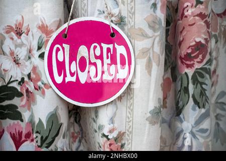 A Sorry we're closed sign displayed on a shop doorway window. The sign is displayed in front of a dulled sun bleached curtain. It has a retro font Stock Photo