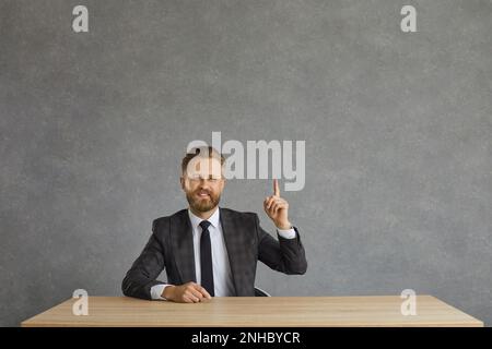Smiling positive businessman in formal suit have idea sit at desk studio shot Stock Photo
