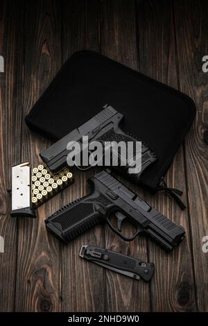 Two small modern 9 mm pistols and cartridges for them lie on a black padded case. Short-barreled firearms for self-defense. Dark wooden background. Stock Photo