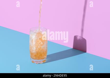 Pouring tea in a glass over the crushed ice, minimalist on a vibrant colored background. Glass with crushed ice and tea on a blue table in a bright li Stock Photo