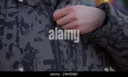 Young man closing his jacket zipper in close-up, cold weather concept Stock Photo