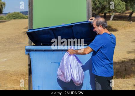 Man throwing garbage bags into a dumpster with a blank sign for copy space Stock Photo