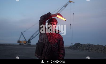 Young Serious Man Waving Red Light by Side of Road and Looking at Camera, Working Concept Stock Photo
