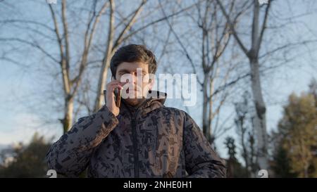 Young Man in Thick Black Coat Engages in a Phone Conversation by Placing his Smartphone to his Ear Stock Photo