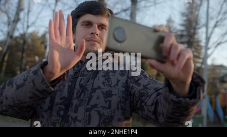 Connecting with the World Outdoors: Young Man Holding His Smartphone Horizontally, Greeting and Video Chatting with Online Friends, Embracing the Free Stock Photo