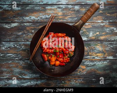 Asian or Chinese style delicious chicken in sweet and sour sauce served in black rustic wok pan on colorful wooden background. Asian dinner concept Stock Photo