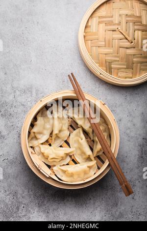 Close-up, top view of traditional Asian dumplings in bamboo steamer with chopsticks on gray rustic stone background. Authentic Chinese cuisine Stock Photo
