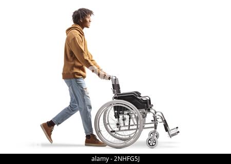 Full length profile shot of an african american young man pushing an empty wheelchair isolated on white background Stock Photo