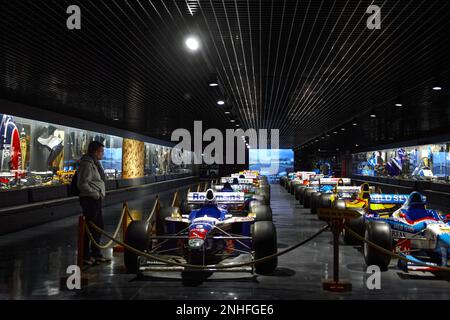 A man standing next to a lot of racing cars in a museum