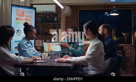 Coworkers brainstorming, african american team analyst showing revenue statistics on laptop screen. People planning strategy in business meeting, discussing analytics presentation Stock Photo