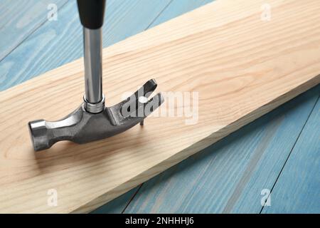 Hammer pulling metal nail out of plank on light blue table, closeup Stock Photo