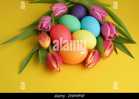 Fresh colorful tulip flowers and easter eggs on yellow background. Happy easter greeting card. Stock Photo