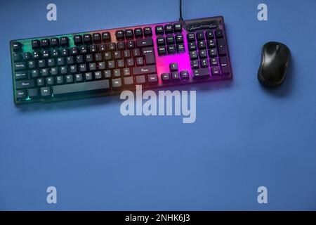 Modern RGB keyboard and mouse on blue background, flat lay. Space for text Stock Photo