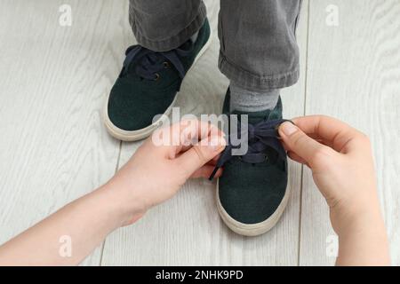 Mother helping son to tie shoe laces at home, closeup Stock Photo