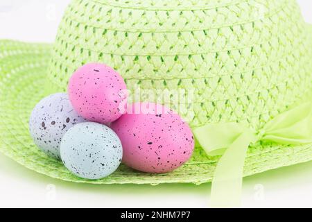 Pair of pink and two blue Easter eggs, all four speckled, placed on pastel green spring bonnet against white background Stock Photo