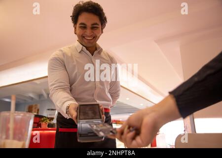 Waiter holding card reader while customer making payment through credit card Stock Photo