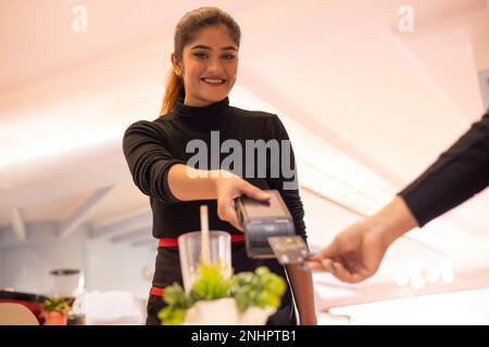 Waitress holding card reader while customer making payment through credit card Stock Photo