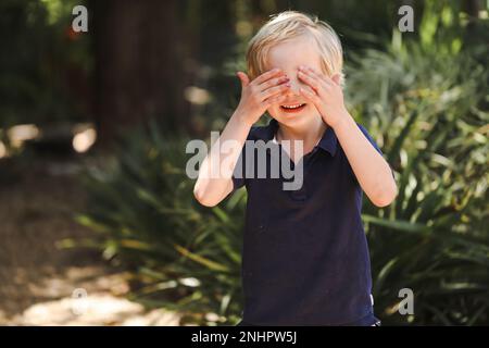 Preschool boy covering eyes, playing hide and seek outdoors at kindergarten Stock Photo