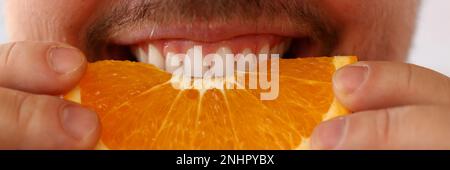 Bearded smiling man holds and bites orange fruit Stock Photo