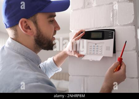 Man installing home security system on white wall in room Stock Photo