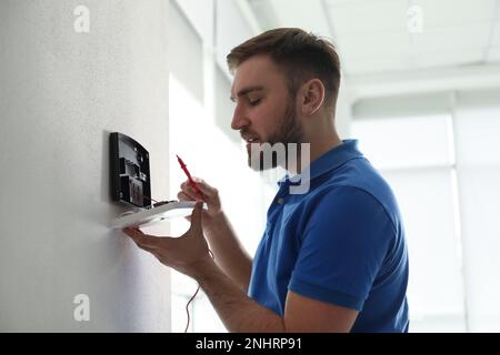 Man installing home security system on white wall in room Stock Photo
