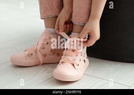 Little girl tying shoe laces at home, closeup Stock Photo