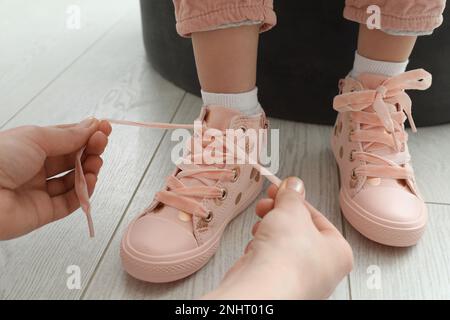 Mother helping daughter to tie shoe laces at home, closeup Stock Photo