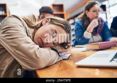 Taking a break is just as important. a university student falling asleep in the library. Stock Photo