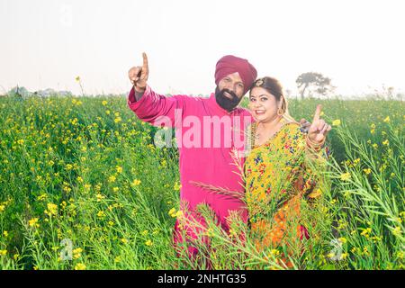 Happy young Punjabi sikh couple standing together do dancing pose at agriculture field. Stock Photo