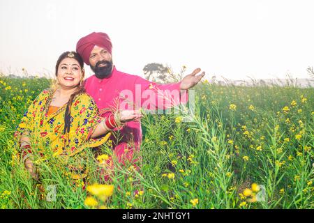 Happy young Punjabi sikh couple standing together at agriculture field. Stock Photo