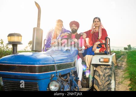 Happy punjabi sikh farmer family driving tractor at agriculture field outdoor. Stock Photo